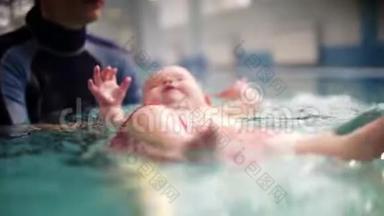 教练或妈妈教宝宝在游泳池游泳.. 婴儿躺在背上，学会保持平衡，继续前进